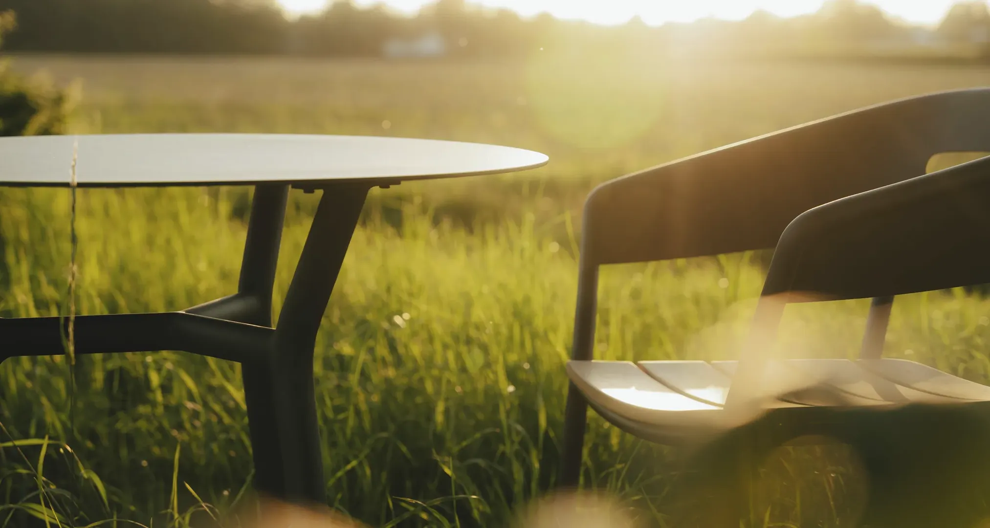 ALTEA Tisch und Gartenstuhl von TRAZOS auf einer Wiese bei Sonnenuntergang“